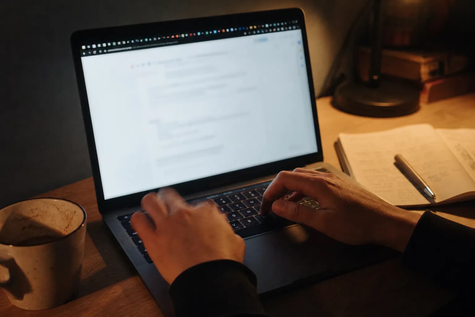 Hands on a laptop keyboard at night with many browser tabs blurred at the top of the screen, a paper notebook and coffee cup on a wooden desk - the agency reality both tools were built to remove
